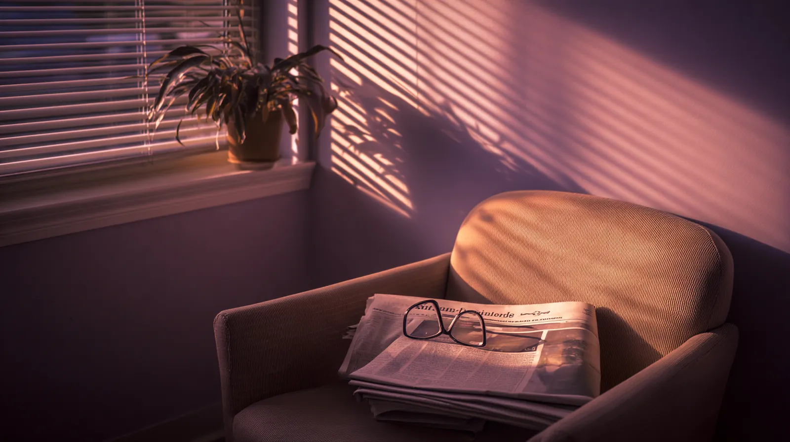An empty waiting-room armchair in late sun through venetian blinds, a folded newspaper and a pair of reading glasses on the seat.
